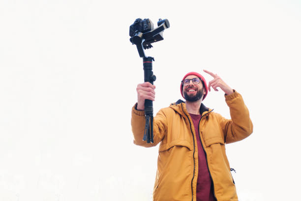 videographer filming himself with a dslr camera on a motorized gimbal with a white background