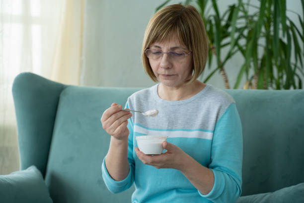 istock Elderly woman eats yogurt sitting on the couch at home 1310227126