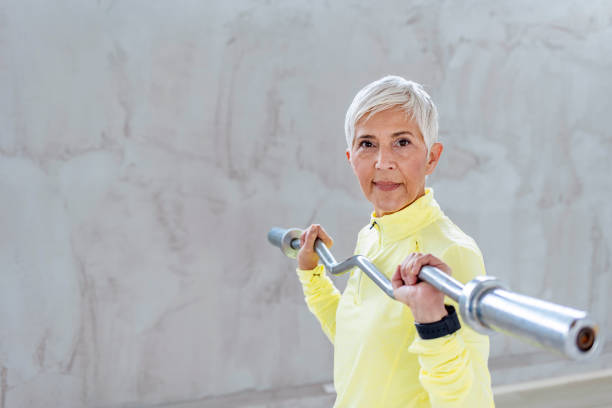 Exercising has had a profound effect on her overall health Shot of a focused senior woman lifting a barbell on her own in the gym, looking at camera. senior bodybuilders stock pictures, royalty-free photos & images