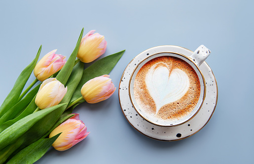 Spring tulips and cup of coffee on a blue background