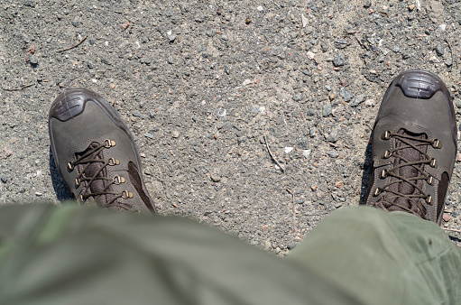 Low Section of the male body in combat boots and trousers. A military soldier stands on the asphalt in brown boots and a green uniform. Outside the premises. View from above.