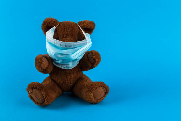 istock Teddy bear toy with medical protective mask on a blue background with copy space. 1310234956