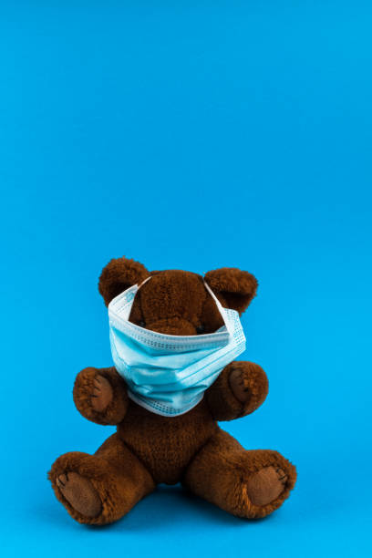 istock Teddy bear toy with medical protective mask on a blue background with copy space. 1310234957