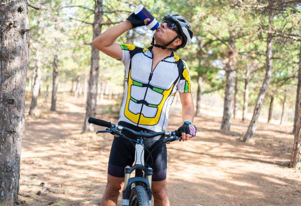 istock Young professional thirsty cyclist drinking water from the bottle in forest 1310235441