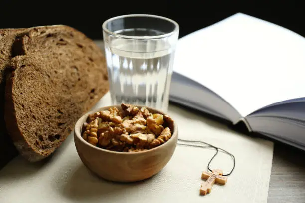 Photo of Bread, walnuts, water, Bible and crucifix on table. Great Lent season