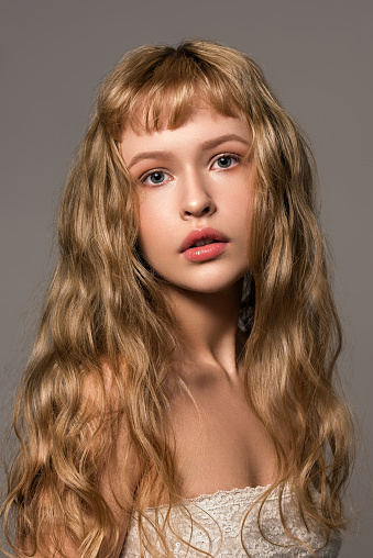 Close up portrait of young fashion model with beautiful natural blond wavy hair and gentle makeup. The concept of healthy clean well-groomed skin. Trendy hairstyle with bangs cut.
