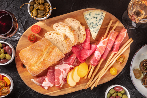 Italian antipasti with hams, cheeses, and bread, overhead shot on a dark background