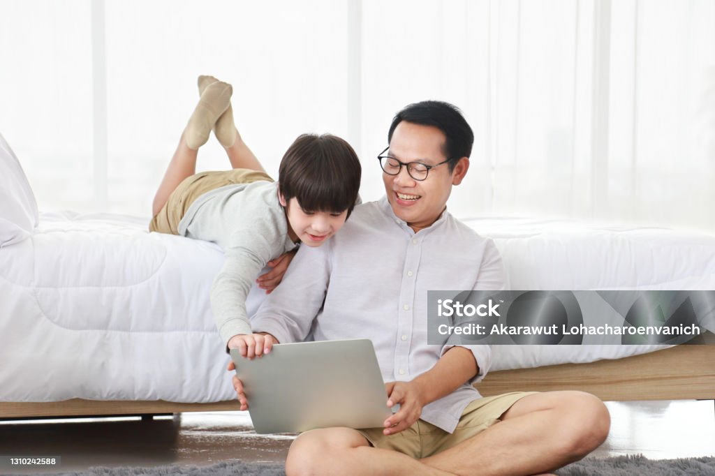 Asian father teaching homework to his son in bed for homeschooling, distance learning and education Asian father teaching homework to his son in bed for homeschooling, distance learning and education concept Asian and Indian Ethnicities Stock Photo