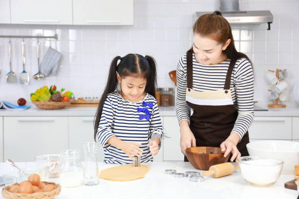 mãe asiática feliz ensinando sua filha jovem em assar pão de massa dentro cozinha branca moderna usando cortador de biscoitos - bread food baked 7 grain bread - fotografias e filmes do acervo