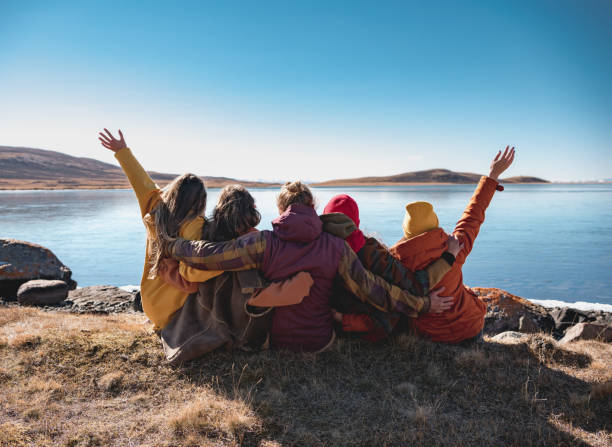 Group of happy friends sitting at mountain lake Group of happy young friends are sitting near mountain lake, hugging and having fun altai republic photos stock pictures, royalty-free photos & images