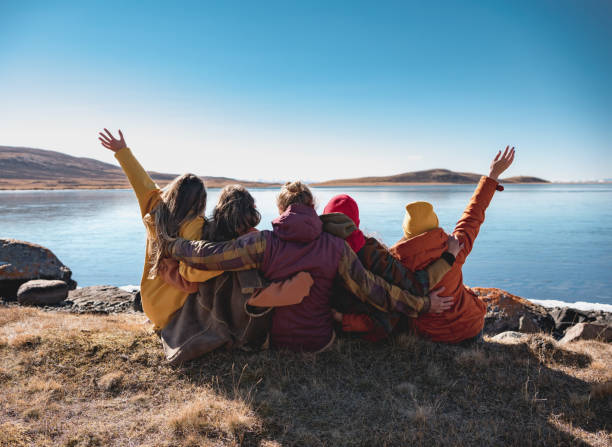 Group of happy friends sitting at mountain lake Group of happy young friends are sitting near mountain lake, hugging and having fun western siberia stock pictures, royalty-free photos & images