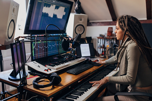 Modern and creative, young  female artist, in her sound recording studio, using the electric music keyboard, while working on audio engineering