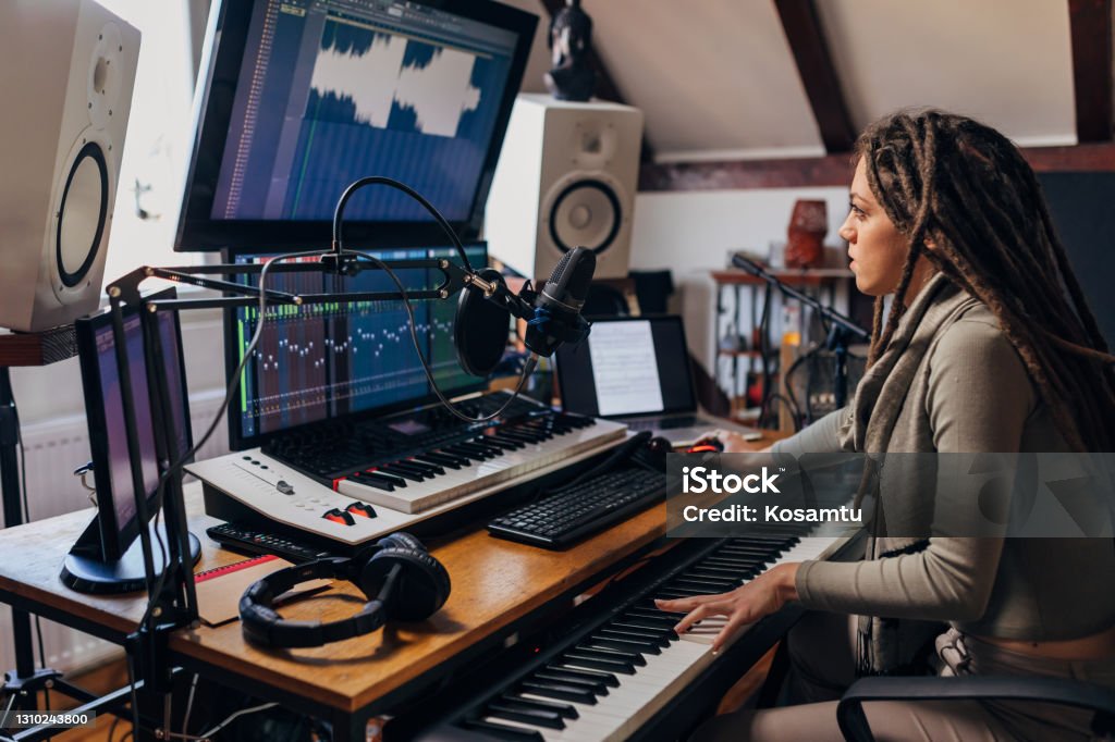 Dedicated young woman, an audio engeener, working on sound mixing from her music and sound record studio Modern and creative, young  female artist, in her sound recording studio, using the electric music keyboard, while working on audio engineering Editing Equipment Stock Photo