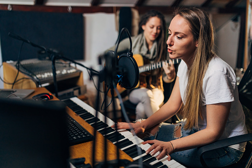 Modern and young female friends, having a band rehearsal , while singing, playing the music keyboard and acoustic guitar in their home music studio