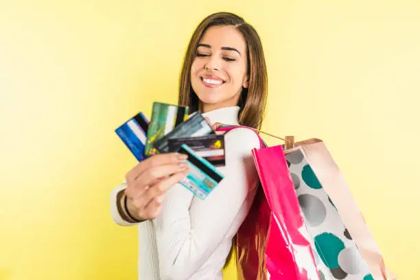 Beautiful happy woman with credit card and shopping bags isolated on yellow background with copyspace. Online Shopping concept