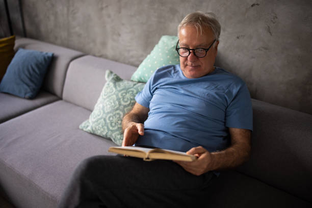 istock Senior man sitting on sofa and reading book while relaxing at home 1310250148
