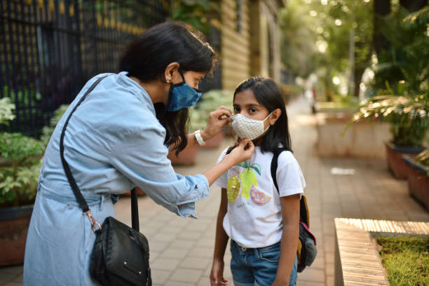 Mother putting protective face mask on her daughter's face