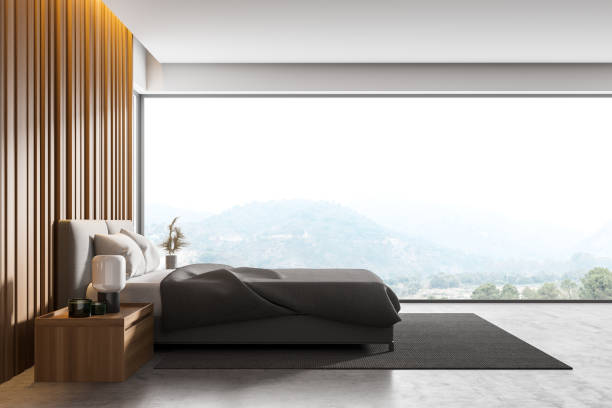 istock Master bedroom with grey wooden walls, panoramic window with countryside view, comfortable king size bed standing on gray carpet and concrete floor. 1310256394