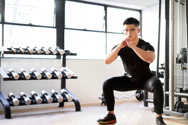 uomo asiatico accovacciato in una palestra di allenamento - crouching foto e immagini stock