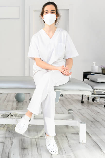 istock Friendly female physiotherapist posing in modern clinic wearing protective face mask during coronavirus pandemic. High quality photo 1310264930