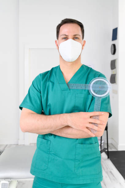 istock Friendly male physiotherapist posing with tools in modern clinic wearing protective face mask during coronavirus pandemic. High quality photo 1310264960