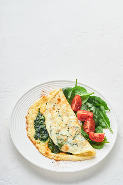 istock Omelet or omelette with spinach, cherry tomato and pepper seasoning on a white plate, on white background. Top view. 1310266592