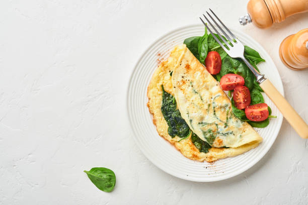 istock Omelet or omelette with spinach, cherry tomato and pepper seasoning on a white plate, on white background. Top view. 1310267168