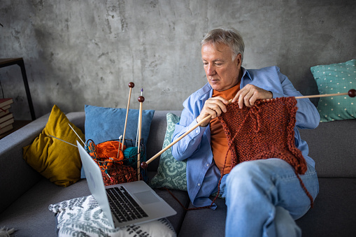 Senior man watching online tutorial to learn to knit at home