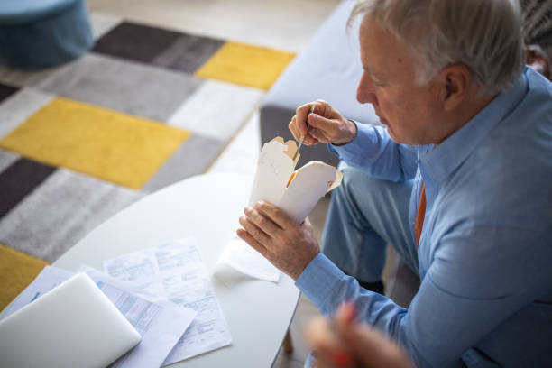 istock Senior man eating pasta from paper box at home 1310267528