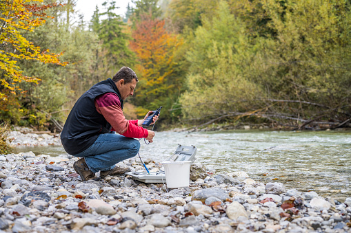 Male biologist using multiparameter instrument while testing dissolved oxygen in river.