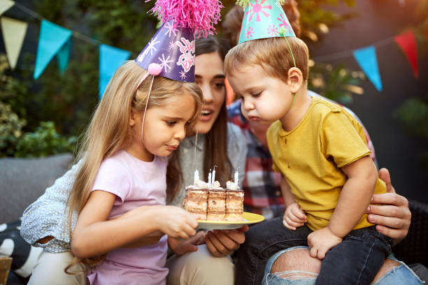 ケーキにろうそくを吹く誕生日帽子を持つ子供たち - birthday family party cake ストックフォトと画像