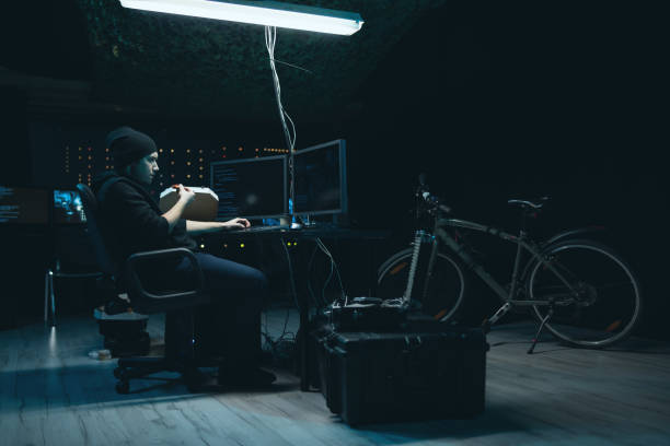 istock A hacker organize an attack on data servers. He hideout is dark and full of operational displays. The guy is taking a break, eating pizza and analyzing the malware code on the computer 1310269809