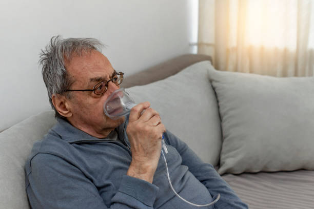 istock Man using inhaler while sitting on sofa at home during the day. 1310269923