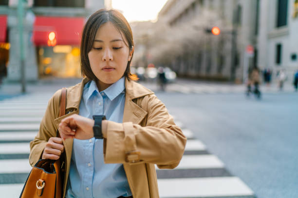 Young business woman commuting and crossing the street in financial district in city A young business woman is commuting and crossing the street in a financial district in the city. smart watch business stock pictures, royalty-free photos & images