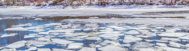 White ice floes under the blue sky. Trees are reflected in the water. Spring melting of ice on the Moscow River. The beginning of the ice drift.