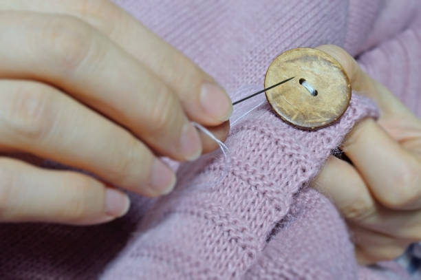 istock female workers' hands sew a wooden button to a jacket. close-up. 1310280537