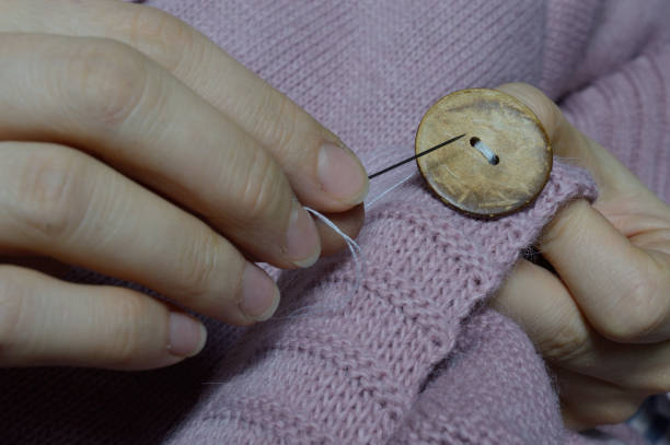 istock female workers' hands sew a wooden button to a jacket. close-up. 1310280538