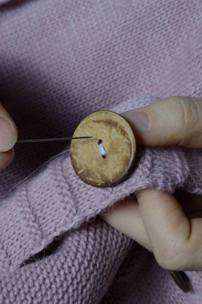 istock female workers' hands sew a wooden button to a jacket. close-up. 1310280573