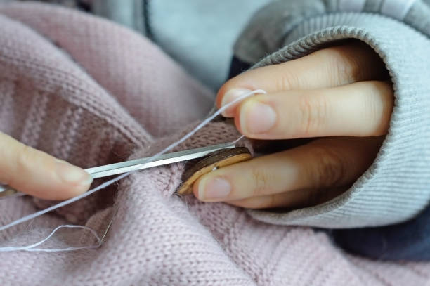 istock female workers' hands sew a wooden button to a jacket. close-up. 1310280637