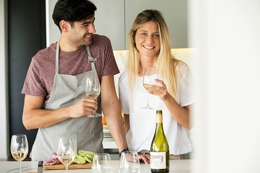 Happy young couple with wine glasses standing together in kitchen