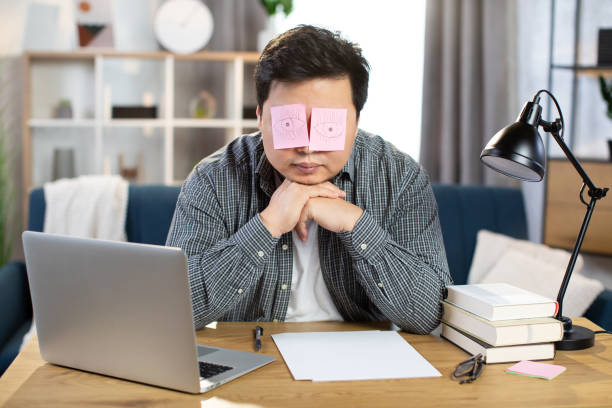 istock Man sleeping at work with fake eyes painted on paper sticker, covered his eyes 1310284726