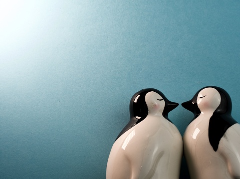 Background of ceramic penguins kissing against light blue background with bright light in top left corner and copy space