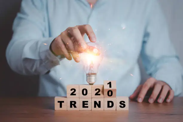 Photo of Businessman holding lightbulb on flipping 2020 to 2021 trends print screen on wooden block cubes. New idea business fashion popular and relevant topics.