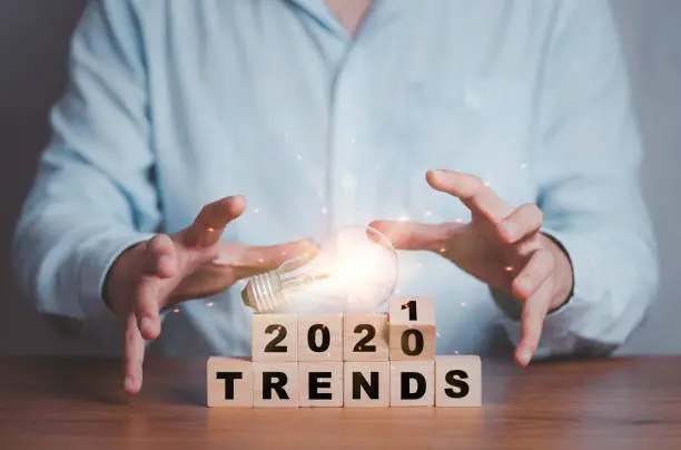 Photo of Businessman holding lightbulb on flipping 2020 to 2021 trends print screen on wooden block cubes. New idea business fashion popular and relevant topics.