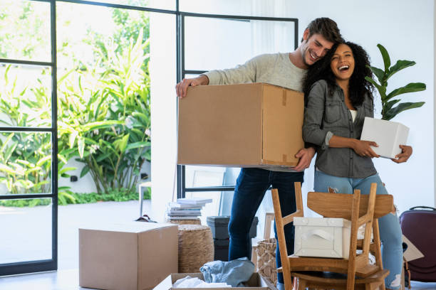 Couple carrying cardboard box and pot plant in new house Happy couple carrying cardboard box and pot plant in new house home ownership stock pictures, royalty-free photos & images