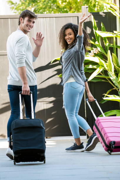 istock Smiling couple walking with carry-on luggage while waving goodbye 1310289365