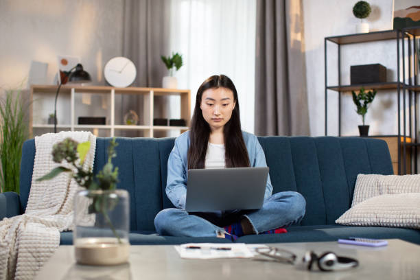 istock Asian woman working on laptop while sitting on sofa 1310289390