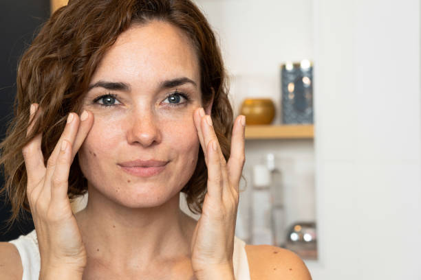 close-up of woman applying cream to her cheeckbones using both hands - wrinkled skin imagens e fotografias de stock