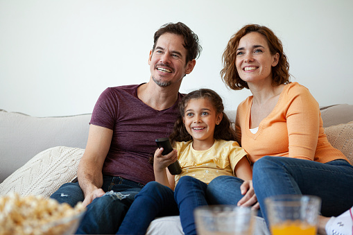 Happy family sitting together on sofa while watching television in living room at home