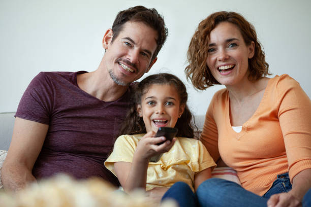 istock Happy family sitting together on sofa and watching television 1310290983